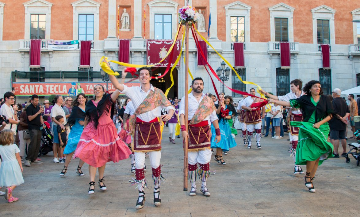 Balladores amb faldilles de colors i mocador negre i balladors amb camisa blanca, faldilla granat i polaines, ballant amb les cintes davant l'Ajuntament