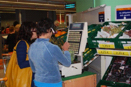 Fotografia d'una de les noies pesant la fruita en el supermercat del barri amb el suport de l'educadora